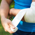 A person in a blue shirt wrapping their arm in tape forming a temporary cast.